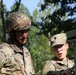 Two U.S. Army soldiers in OCP (Operational Camouflage Pattern) uniforms are engaged in what appears to be a training or operational activity near a military vehicle. The soldier on the left, identified by the name tape 'BOVE', is wearing a combat helmet and glasses, while the soldier on the right, identified as 'FOSTER', is wearing a patrol cap and safety glasses. Both soldiers appear to be examining or operating equipment on a green military vehicle.