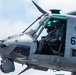 A close-up photograph of a military attack helicopter, specifically appearing to be a Bell AH-1Z Viper, with bureau number 61 visible on the fuselage. Two crew members in flight suits and helmets with night-vision equipment are visible in the tandem cockpit. The aircraft is airborne and the name 'CAPT J.J. BALLERINO TOLENTINO' is stenciled on the cockpit frame.