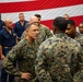 A senior U.S. Marine Corps officer with the name tape 'DONOVAN' and general officer rank insignia is engaged in conversation with two Marines in MARPAT camouflage uniforms. The setting appears to be aboard a naval vessel or military facility, with a large American flag displayed prominently in the background. Navy personnel in blue coveralls are visible standing in the background.