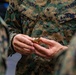 A U.S. Marine wearing MARPAT digital camouflage uniform with the name tape 'DONOVAN' is holding a gold rank insignia device, likely during a promotion or award ceremony. The insignia appears to be a First Sergeant or Sergeant Major chevron device based on its shape and gold color. Another Marine's hands are visible receiving or presenting the insignia.