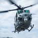 Two military helicopters are operating on the flight deck of a naval vessel at sea. The foreground helicopter, numbered '61', is airborne and hovering low over the deck, while a second helicopter numbered '67' remains on the deck in the background. Both aircraft appear to be UH-1Y Venom helicopters used by the United States Marine Corps.