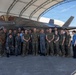 A group of approximately 25 military personnel pose for a formal group photograph in front of an F-35 fighter jet under a hangar shelter. The group includes members wearing multiple uniform types, suggesting a multinational or joint-service gathering. The setting appears to be a military airfield or flight line.