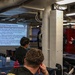 A military briefing or training session is taking place aboard what appears to be a naval vessel, with a presenter standing near a projected slide titled 'Better Living Through Chemistry.' The presentation covers neurochemicals including Endorphins, Dopamine, Oxytocin, and Serotonin and their roles in well-being. Several uniformed and civilian personnel are seated at tables facing the presenter and projection screen.