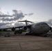 A U.S. Air Force C-17 Globemaster III military transport aircraft, tail number 5146, is parked on a tarmac at dusk or dawn. The aircraft bears markings indicating assignment to the 15th Wing and 154th Wing. Ground crew personnel and support equipment are visible around the aircraft, suggesting pre-flight or post-flight servicing operations.