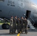 Five U.S. Air Force personnel in flight suits pose together in front of a large military aircraft marked '1104' and '97 AMW' (Air Mobility Wing). The group is standing on a tarmac beneath the fuselage of what appears to be a C-17 Globemaster III, with the aircraft's entry stairs visible to the right. The image appears to be an official or commemorative crew photo.