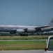 A U.S. Air Force KC-135 Stratotanker aerial refueling aircraft is taxiing or taking off on a runway. The aircraft bears the tail number 23528 and AMC (Air Mobility Command) markings, along with a U.S. flag on the tail. The setting appears to be a military or joint-use airfield surrounded by green vegetation under clear skies.