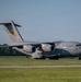 A U.S. Air Force C-17 Globemaster III military cargo aircraft is taxiing on a runway or taxiway. The aircraft bears tail number 21104 and unit designation '97 AMW' (Air Mobility Wing), painted in standard military gray livery. The photo was taken during golden hour lighting conditions at what appears to be a military or civilian airfield.