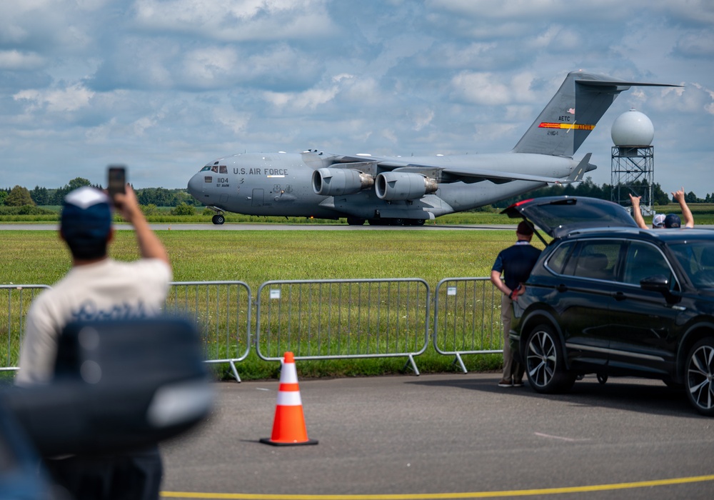 A U.S. Air Force C-17 Globemaster III military transport aircraft is taxiing on a runway while spectators observe and photograph it from behind a security barrier. The aircraft bears the markings 'AETC' (Air Education and Training Command) on its tail fin and the serial number 804. The scene appears to be at an airshow or public aviation event, with civilians gathered near a parked SUV to watch.