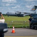 A U.S. Air Force C-17 Globemaster III military transport aircraft is taxiing on a runway while spectators observe and photograph it from behind a security barrier. The aircraft bears the markings 'AETC' (Air Education and Training Command) on its tail fin and the serial number 804. The scene appears to be at an airshow or public aviation event, with civilians gathered near a parked SUV to watch.