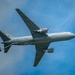 A U.S. Air Force military tanker aircraft is photographed from below against a partly cloudy blue sky. The aircraft is a KC-46 Pegasus (Boeing 767-based tanker) in standard gray military livery, with serial number 66018 visible on the fuselage. The image captures the underside of the aircraft in flight, showing its twin-engine configuration and aerial refueling boom extended beneath the tail.