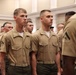 A group of U.S. Marine Corps personnel standing in formation in what appears to be an indoor ceremonial or administrative setting. The individuals are wearing the standard khaki/tan Service Charlie uniform with olive drab trousers. The two foreground Marines display Private First Class rank insignia on their collars.