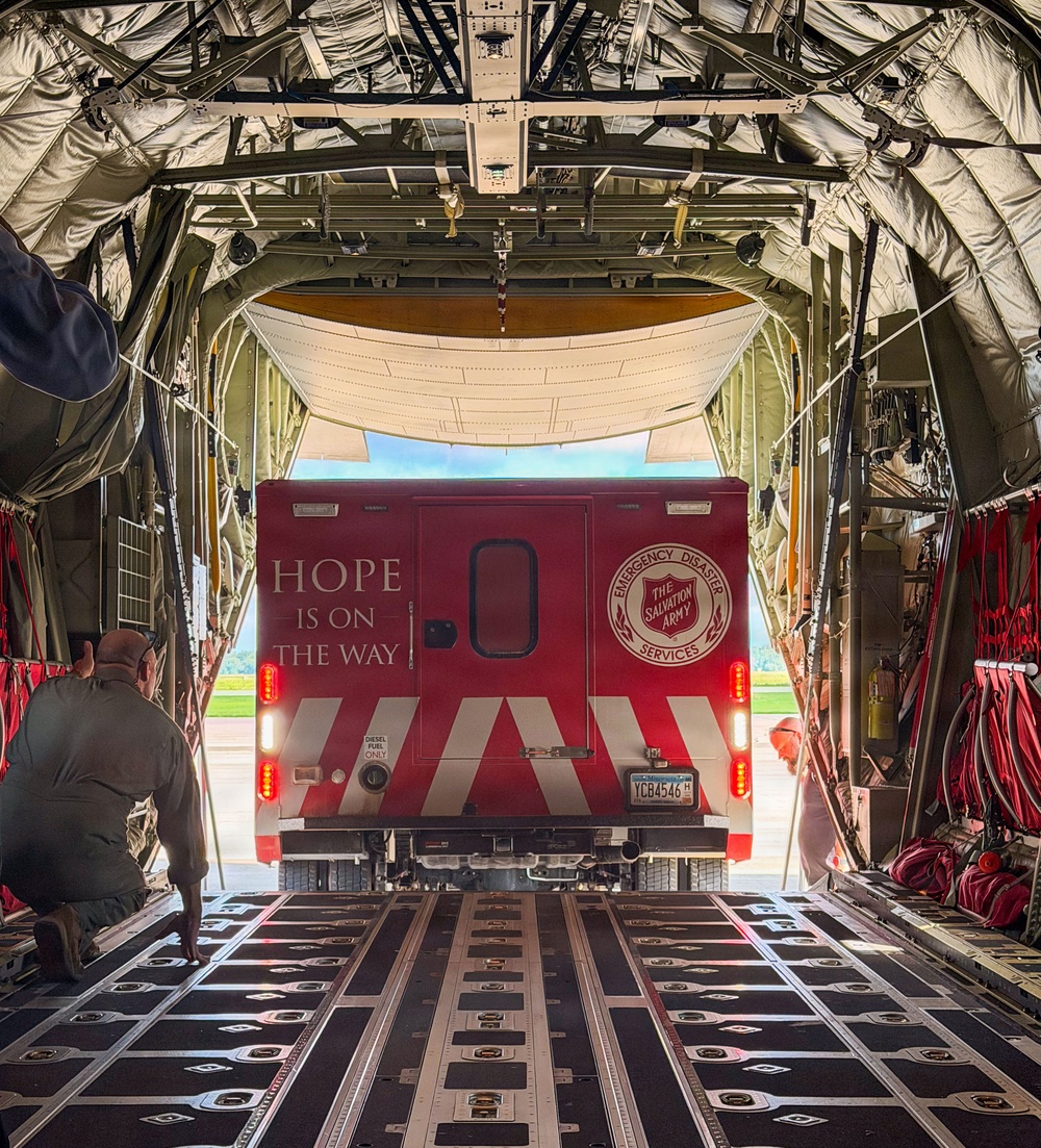 A Salvation Army Emergency Disaster Services vehicle is being loaded into or unloaded from a large military cargo aircraft, likely a C-130 Hercules. The red vehicle bears the text 'HOPE IS ON THE WAY' and the Salvation Army shield logo on its rear doors. A person in military-style clothing is kneeling on the cargo ramp, likely guiding the vehicle's positioning.