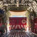 A Salvation Army Emergency Disaster Services vehicle is being loaded into or unloaded from a large military cargo aircraft, likely a C-130 Hercules. The red vehicle bears the text 'HOPE IS ON THE WAY' and the Salvation Army shield logo on its rear doors. A person in military-style clothing is kneeling on the cargo ramp, likely guiding the vehicle's positioning.