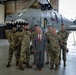 A group of seven military personnel in OCP (Operational Camouflage Pattern) uniforms pose with one civilian in a gray suit and red tie inside an aircraft hangar. They are standing in front of an A-10 Thunderbolt II (Warthog) attack aircraft featuring a distinctive shark mouth nose art. A unit patch/emblem is visible on the aircraft's tail section.