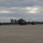 Multiple military helicopters are parked on a concrete flight line or tarmac under an overcast sky. The helicopters appear to be UH-72 Lakota (Eurocopter EC145) utility helicopters in olive drab/dark military paint schemes. The setting appears to be a military airfield with a tree line visible in the background.