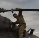 A soldier in MultiCam/OCP camouflage uniform is performing maintenance or inspection on top of a military helicopter. The aircraft has 'Kentucky' written on its fuselage, indicating it belongs to the Kentucky National Guard. The soldier is gripping a main rotor blade while positioned on top of the aircraft under an overcast sky.