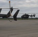 The image shows multiple military helicopters on a tarmac or airfield under an overcast sky. At least three UH-72 Lakota helicopters are visible, with one appearing to be in the process of landing or hovering in the background. The helicopters are painted in standard U.S. Army olive drab/dark gray livery.