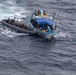 An aerial photograph shows a rigid inflatable boat (RIB) alongside a larger fishing vessel named 'Los Tres Hermanos' on open ocean waters. The RIB appears to be operated by uniformed personnel who have pulled alongside the fishing vessel, suggesting an interdiction or boarding operation. Multiple people are visible aboard the fishing vessel, which is blue and white in color.