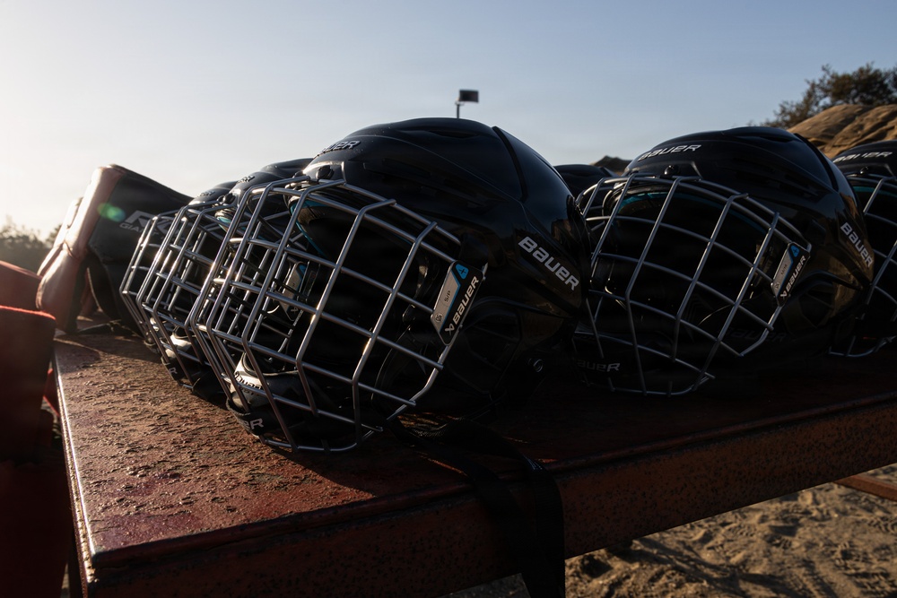 Multiple black Bauer hockey helmets with wire cage face guards are lined up on what appears to be a metal railing or bench. The helmets are photographed in an outdoor setting with natural backlighting creating a dramatic silhouette effect. The image appears to be taken at a hockey facility or outdoor rink area.