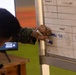 A person in camouflage military uniform is writing on a whiteboard with a blue marker. The whiteboard contains a table with column headers including 'TARGET #', 'LAUNCHER', and 'MAX ORD' (partially visible). Visible entries include 'ERMEC-900' and '520NMH' among other partially legible text.