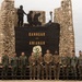 A group of military personnel pose in front of a memorial monument inscribed with 'BANNUAR ITI AMIANAN,' which translates from Ilocano (Filipino dialect) to 'Hero of the North.' The monument features stone pillars, silhouetted soldier figures, a battlefield cross, and a commemorative wreath, suggesting a joint military ceremony. The group includes both Philippine Armed Forces soldiers and what appear to be U.S. Marines in different camouflage uniforms.