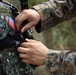 Two military personnel are shown in close interaction, with one adjusting or inspecting equipment on the other. The soldier on the left wears a 'Philippine Marines' patch with a Philippine flag insignia, while the soldier on the right wears USMC MARPAT digital camouflage. This appears to depict a joint training or cooperative military exercise between Philippine Marines and U.S. Marines.