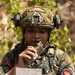 A Philippine Marine soldier is captured in the field reading from a handwritten notepad while communicating via a handheld tactical radio. The soldier is wearing full combat gear including a FAST helmet with ear protection and NVG mount, digital camouflage uniform, and tactical vest. Patches on the uniform identify the individual as a member of the Philippine Marines and the Marine Corps Beachhead unit (2008).