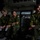 Three young soldiers in Swedish military camouflage uniforms are seated inside what appears to be a military vehicle or command post interior. They are wearing identical M90 pattern camouflage uniforms with visible Swedish flag patches on their shoulders. The setting appears to be the interior of an armored personnel carrier or similar military vehicle.