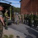A group of military personnel in two distinct camouflage uniforms are gathered in a parking area next to a military van with its rear doors open. The group appears to include both US Marines (in MARPAT digital camouflage) and what appear to be Swedish Armed Forces soldiers (in Swedish M90 camouflage pattern). The setting appears to be a military installation, likely during a joint training exercise or exchange program.