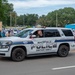 A Wakefield Police Department SUV patrol vehicle is participating in what appears to be a community parade or public event. An officer inside the vehicle is waving to bystanders lined along the street. The scene depicts a positive community-police interaction in a small-town setting.