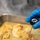A food service worker wearing a blue nitrile glove is using an AVATEMP digital instant-read thermometer to check the internal temperature of cooked chicken in a stainless steel baking pan. The thermometer display appears to read approximately 165°F, which is the USDA-recommended safe internal temperature for poultry. This appears to be a food safety compliance check in a commercial or institutional kitchen setting.