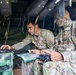 Two U.S. Army soldiers are working inside what appears to be a military command vehicle or tactical operations center. The soldier on the left is operating a ruggedized laptop displaying what appears to be a map or terrain visualization, while the soldier on the right holds a handheld device and references a paper map. Both are wearing Operational Camouflage Pattern (OCP) uniforms in what appears to be a field training or operational environment.