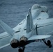 A U.S. Navy carrier-based jet aircraft, marked with the modex number '301', is captured in close-up from a rear-quarter angle, appearing to be in the process of launching from or recovering aboard an aircraft carrier over open ocean. The aircraft displays twin engines, twin tail fins, and deployed landing gear, consistent with a Boeing F/A-18E/F Super Hornet configuration. The ocean is visible in the background, indicating the vessel is at sea.