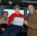 Three individuals are posing for a photo aboard what appears to be a U.S. Navy vessel's bridge or command area. The person in the center is holding a certificate that reads 'Sailor of the Day' dated 19 August 2020, awarded to 'Jackeline C. Noguez-Bruyier' from USS Carl Vinson (CVN-70). Two personnel in military attire flank the award recipient.