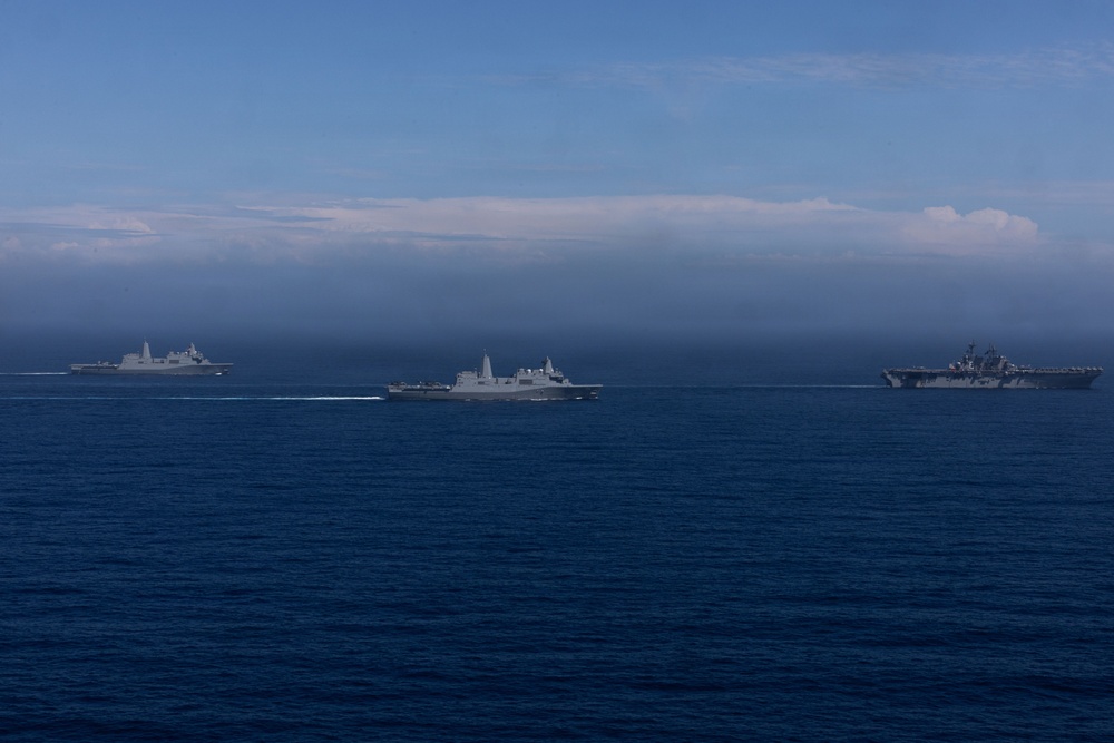 Three gray military naval vessels are sailing in formation across open deep-blue ocean waters. The ships appear to be modern warships, likely belonging to the same naval force or conducting a joint exercise. The scene is photographed from a distance, with a partially cloudy horizon and blue sky in the background.