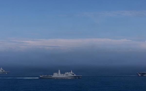 Three gray military naval vessels are sailing in formation across open deep-blue ocean waters. The ships appear to be modern warships, likely belonging to the same naval force or conducting a joint exercise. The scene is photographed from a distance, with a partially cloudy horizon and blue sky in the background.