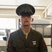 A young male United States Marine is photographed in Service Alpha (Dress Green) uniform inside what appears to be a military barracks. He is wearing the rank insignia of a Private First Class (PFC) on both sleeves and a Rifle Expert badge on his chest. The image is a sharp, well-lit portrait-style photograph taken in an indoor military setting.