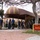 A group of civilians and uniformed military personnel are gathered outside Duncan Hall, a building with a distinctive dome-shaped awning in maroon and gold stripes. The scene appears to depict a military processing or orientation event, with civilians lined up and military personnel in camouflage uniforms overseeing the activity. A red and yellow 'Duncan Hall' sign is prominently visible in the foreground.