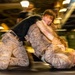The image shows two individuals in military camouflage uniforms engaged in a ground combat training exercise. One person is mounted on top of the other in a grappling position, consistent with martial arts or combatives training. The image uses intentional motion blur (slow shutter speed technique) to convey dynamic movement.