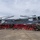 LCF-24 and RS Fort Lauderdale Poolee Function A large group of military personnel and civilians in red shirts pose for a group photograph in front of a U.S. Marines MV-22 Osprey tiltrotor aircraft on a tarmac. The aircraft displays the tail code 'YM' and number '8235', along with a unit insignia on the tail fin, identifying it as belonging to VMM-265. The setting appears to be an outdoor airfield with overcast skies and tropical vegetation visible in the background.