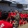 LCF-24 and RS Fort Lauderdale Poolee Function A U.S. Marine in camouflage uniform addresses a large group of young people wearing matching red 'Marines' t-shirts and black shorts, gathered in front of a military tiltrotor aircraft. The aircraft visible in the background is an MV-22 Osprey marked with 'VMM-365' squadron designation and U.S. Marines insignia. This appears to be a recruiting or youth outreach event conducted by the United States Marine Corps.