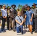 A group of people pose around a bronze memorial statue depicting a Buffalo Soldier standing with a rifle and a horse. Several individuals are wearing distinctive black leather vests with yellow shirts bearing patches that read 'NABS MC' and 'Buffalo Soldiers,' indicating membership in a Buffalo Soldiers motorcycle club. One man kneels in the foreground in front of the statue, suggesting this may be a dedication or commemorative event.