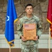 A U.S. Army soldier named Tangen stands at attention holding a wooden award plaque. The plaque reads 'Region VI NCO of the Year 2026' and features an engraved American flag and a map of northwestern U.S. states along with Army National Guard insignia. The soldier is flanked by two ceremonial flags in what appears to be a formal military building interior.