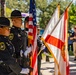 A Hillsborough County Sheriff's Office color guard is presenting flags at an outdoor ceremony. Officers in formal dress uniforms carry the American flag and the Florida state flag, with rifles at ceremonial positions. Additional law enforcement personnel and civilians are visible in the background.