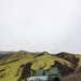 A military wheeled vehicle designated 'STRIKEMASTER' is parked on dark volcanic terrain against a backdrop of moss-covered green hills under an overcast sky. The vehicle appears to be a modern multiple launch rocket system (MLRS) or artillery platform mounted on an armored wheeled chassis, painted in olive/military green. The landscape strongly resembles Iceland's volcanic highland terrain.