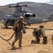 U.S. Marines conduct a forward arming and refueling point (FARP) operation with a UH-1Y Venom helicopter on an arid training field. Personnel in full combat gear are managing fuel hoses and equipment around the idling helicopter, with rotor blades visibly spinning. The setting appears to be a military training installation in a dry, hilly landscape consistent with Southern California.