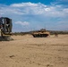 A military beach landing operation is depicted, showing a Landing Craft Air Cushion (LCAC) hovercraft numbered '78' on the left and a wheeled armored fighting vehicle in desert camouflage in the center-background. Several military personnel are visible near the armored vehicle on a sandy beach terrain. The scene appears to be an amphibious assault exercise or operation.