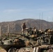 Military personnel in desert camouflage uniforms are positioned atop what appear to be LAV-25 (Light Armored Vehicle) armored vehicles during what appears to be a training exercise. The scene is set in an arid, hilly terrain consistent with a military training installation in the southwestern United States. Multiple vehicles are visible with various equipment, antennas, and gear loaded on them.