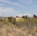 The image shows military vehicles partially concealed by camouflage netting in a dry, scrubby field. Multiple armored vehicles are positioned together with radio antennas extending vertically, suggesting a command or tactical position. The vehicles are heavily draped with camouflage material to blend into the surrounding terrain.