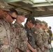 A group of military personnel in camouflage uniforms are standing in a line with heads bowed, suggesting a moment of prayer or solemn ceremony. The group includes both U.S. Army soldiers, identifiable by their OCP (Operational Camouflage Pattern) uniforms and American flag patches, and at least one soldier in what appears to be a Republic of Korea (ROK) Army uniform. The setting appears to be an outdoor covered structure, indicating a formal military event or ceremony.